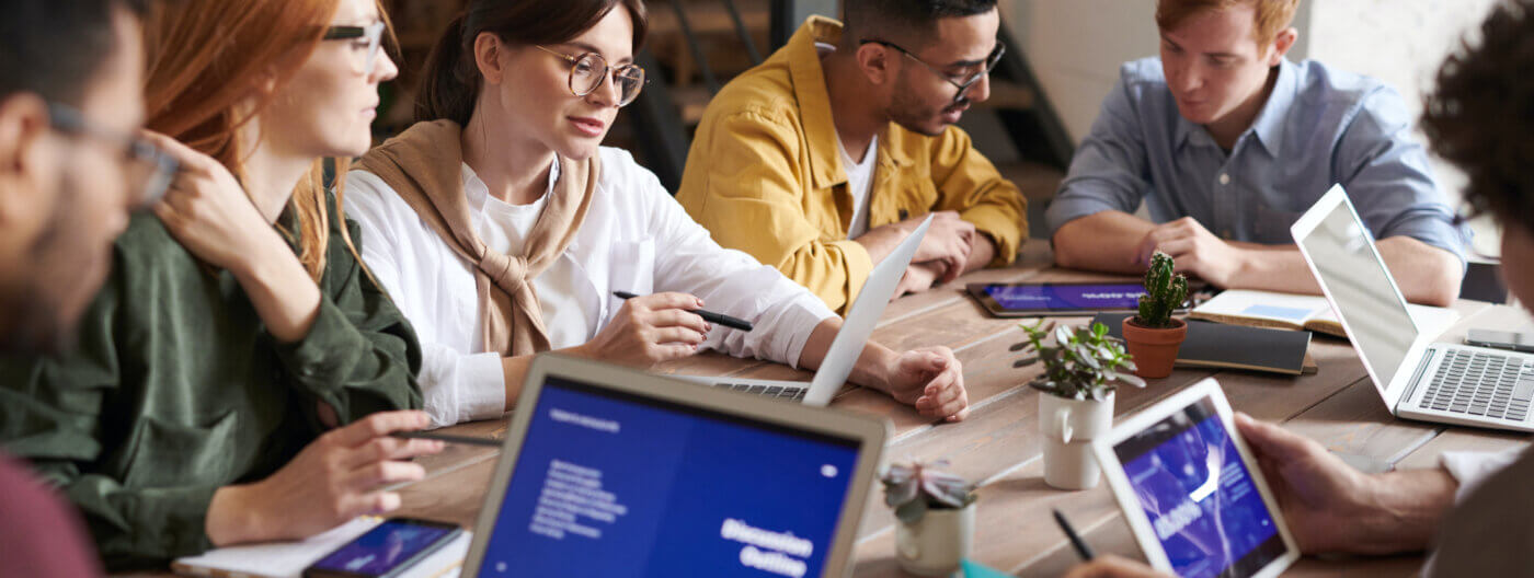 Office table full of employees each looking at computers during a meeting