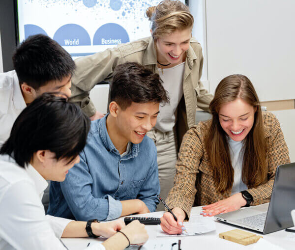 Group of 5 employees around a work desk having a meeting and smiling